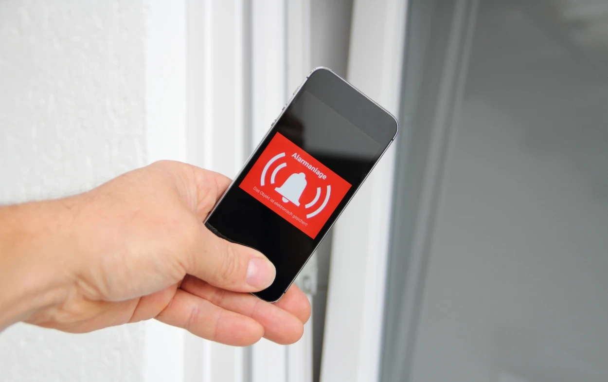 understanding the risks why you need an alarm system Hand holding phone showing alarm notification.